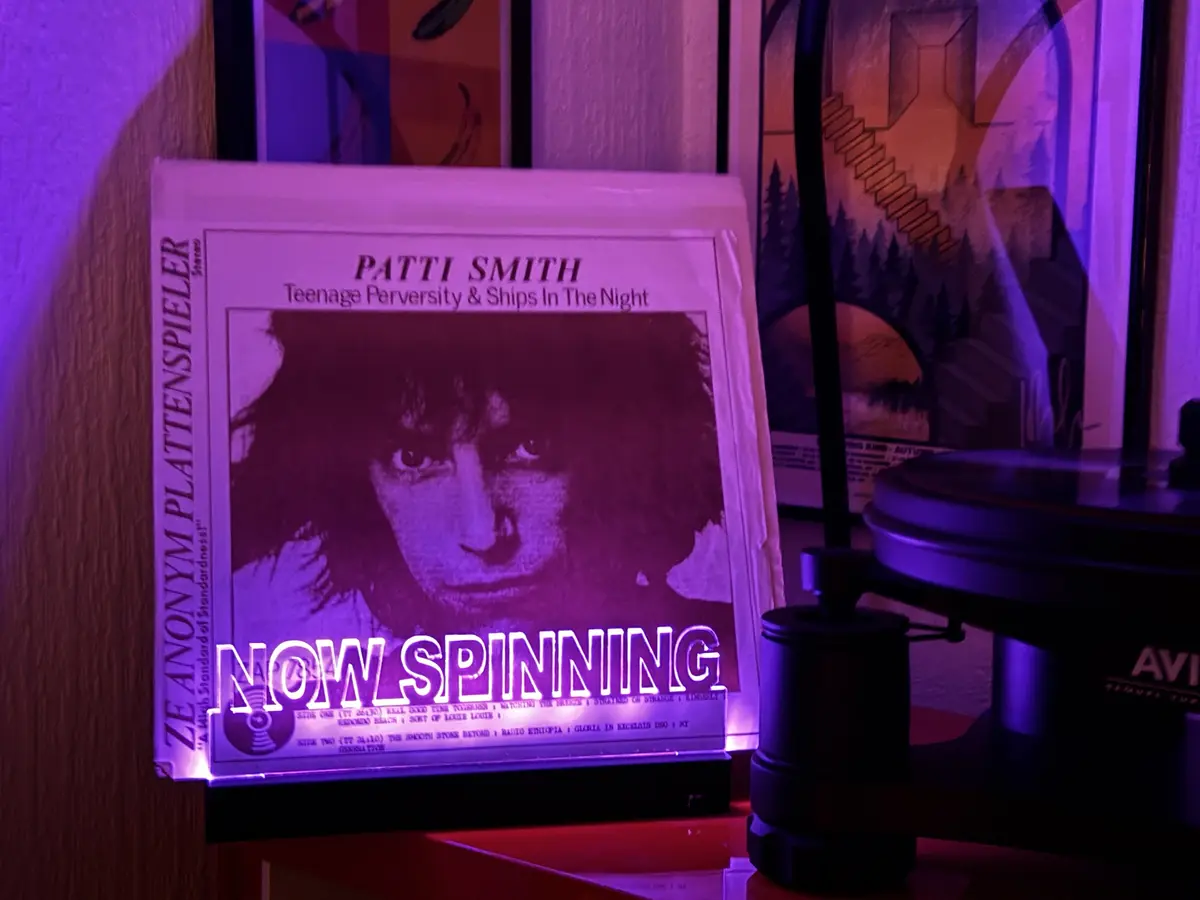 A vinyl record sleeve for Patti Smith's 'Teenage Perversity & Ships In The Night' is displayed next to a turntable under…