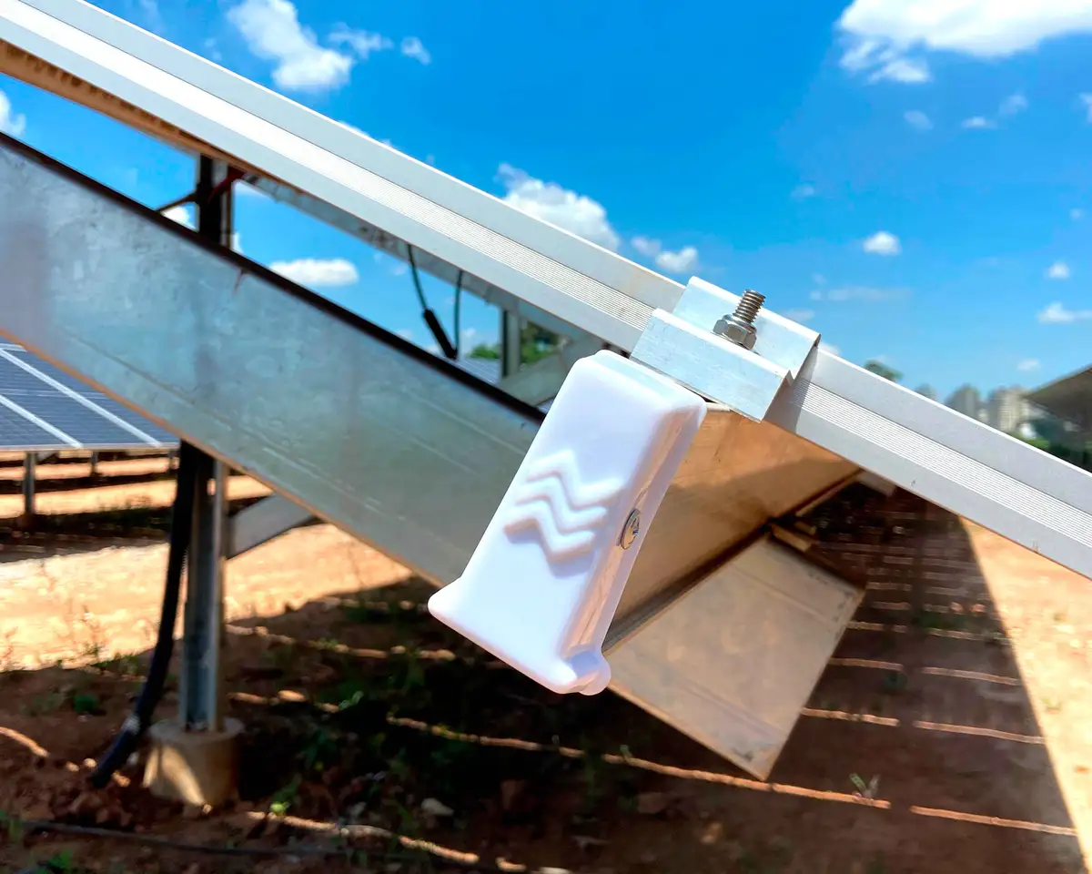 A close-up photo shows a white plastic solar panel mounting bracket with a zigzag pattern, attached to a metal rail under a…
