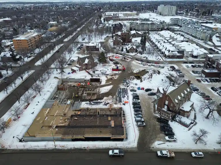 An aerial photo shows a large construction site in a snowy urban neighborhood, surrounded by residential buildings and…