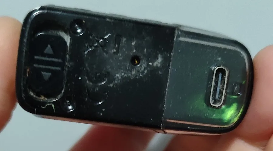 a close-up photo shows a black, worn USB flash drive being held between fingers, with a car key fob-style button panel on…