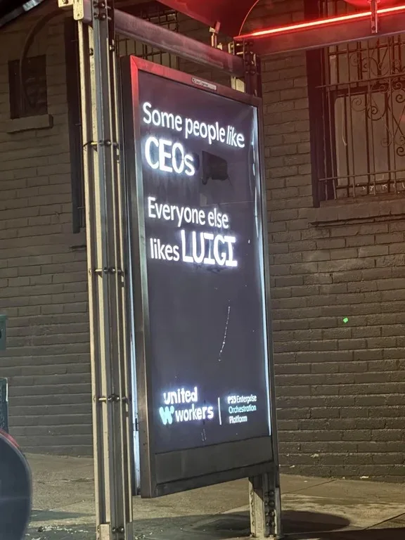 A nighttime photo of a digital billboard on a brick building, displaying white text on a dark background. The text reads…
