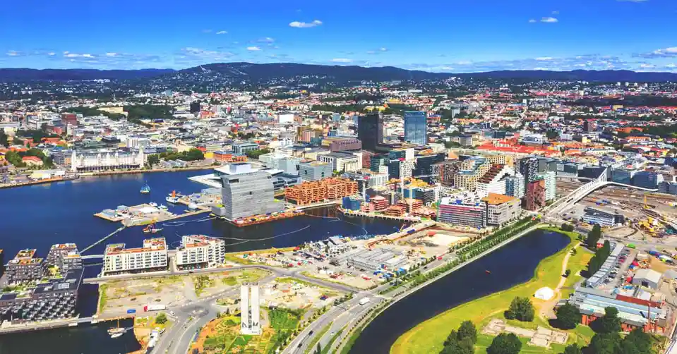 an aerial photograph of a modern cityscape with a harbor, numerous buildings, and visible construction zones with cranes and…
