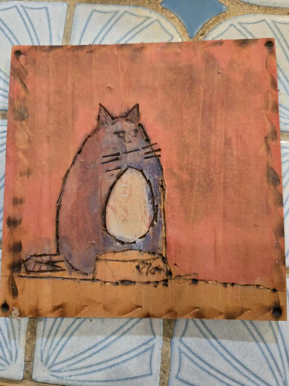A hand-drawn, stylized cat with a round belly and a stern expression sits atop a small pedestal on a wooden plaque. The…