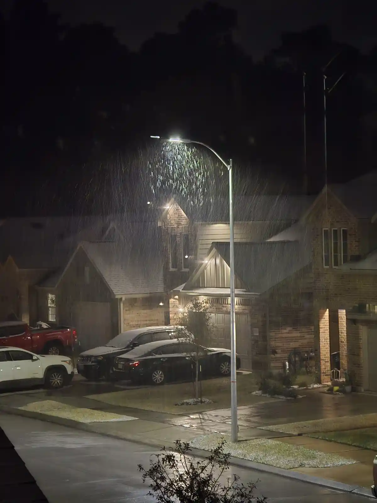 A nighttime photo of a residential street during heavy rain, where a streetlight is so intensely illuminated that it makes…