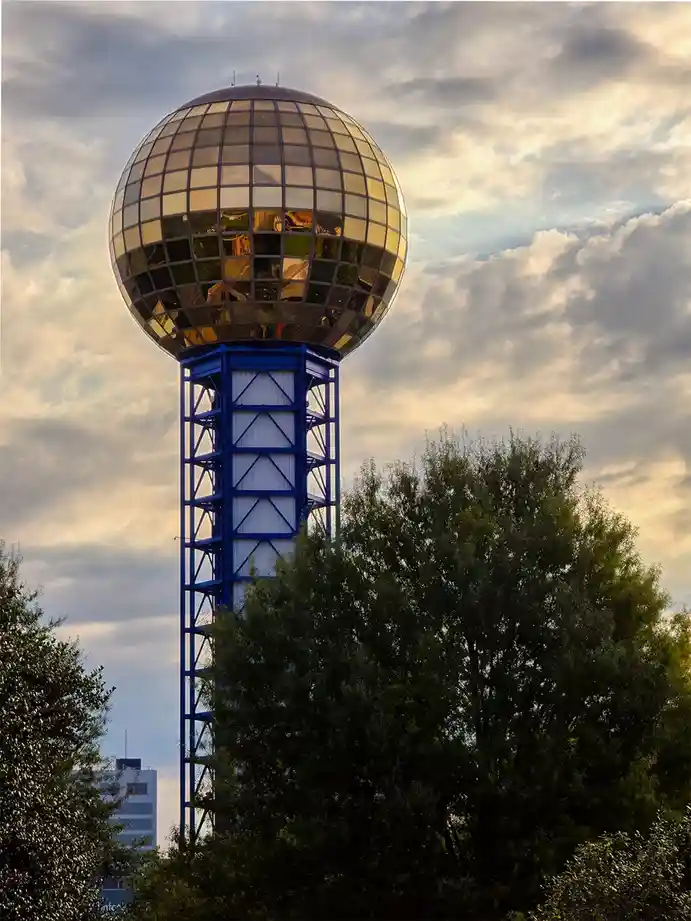 A tall blue metal tower supports a large, reflective, segmented glass globe against a cloudy sky, partially obscured by…