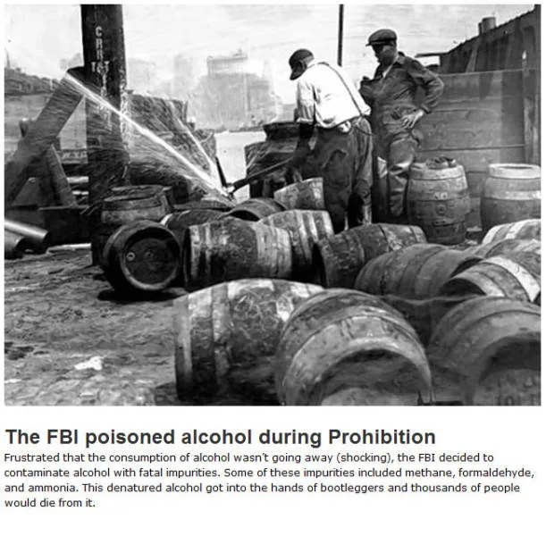 A black-and-white historical photo shows two men in work clothes spraying a liquid from a hose onto a pile of wooden…