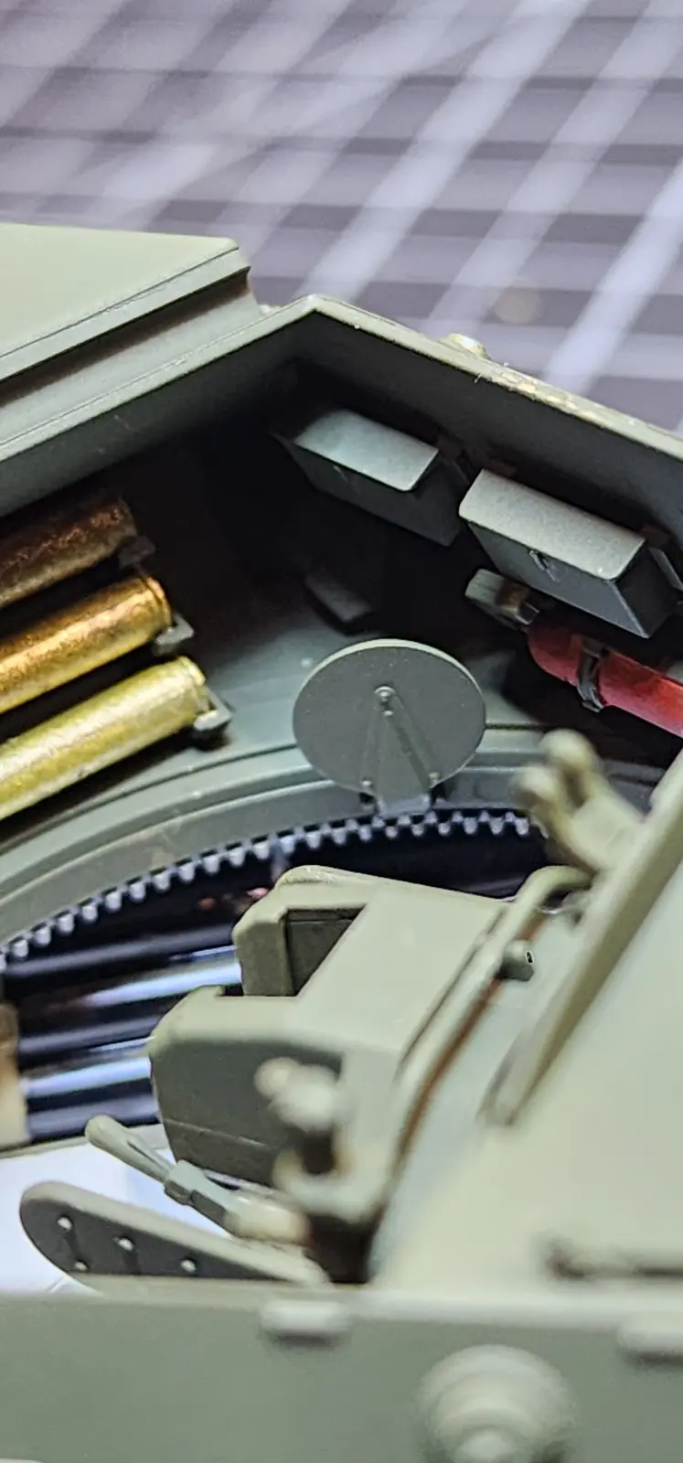A close-up photo of the internal mechanism of a model machine gun, showing brass-colored ammunition, gears, and metal parts…