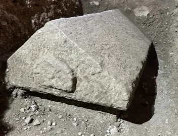 A large, rough-hewn stone block lies on a dirt and gravel surface, appearing heavy and unrefined. Overlaid text reads 'i'm…