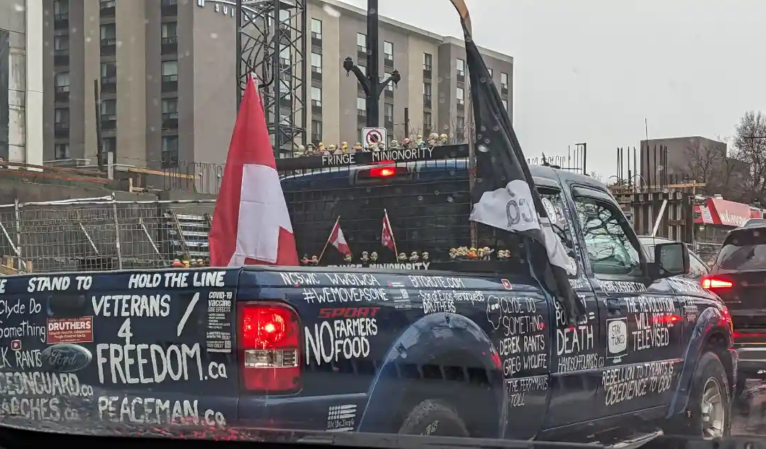A dark blue pickup truck is covered in white spray-painted political slogans and hashtags, including 'Veterans 4…