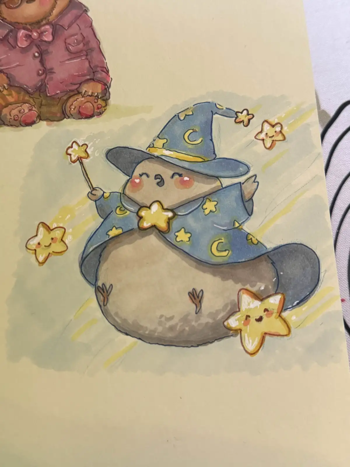 A watercolor illustration shows a chubby, brown, potato-like creature wearing a blue wizard hat and robe decorated with…