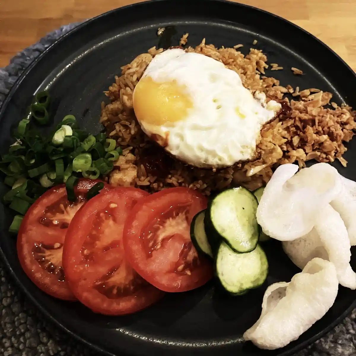 A close-up photo of a black plate holding a meal of fried rice topped with a sunny-side-up egg, accompanied by sliced…