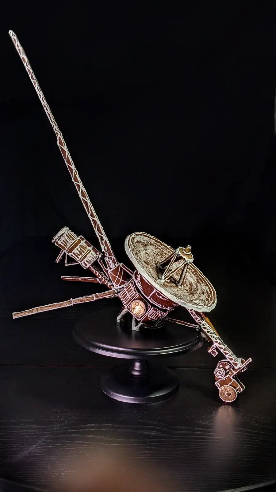 A detailed gingerbread model of the Voyager spacecraft, complete with a dish antenna, long booms, and intricate icing…