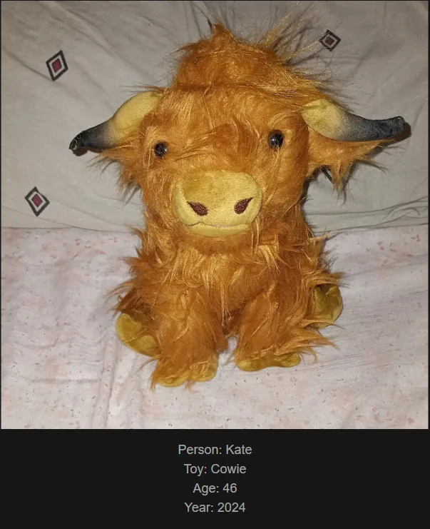 A plush toy resembling a Highland cow with shaggy brown fur, curved horns, and a yellow snout sits on a patterned bedspread…