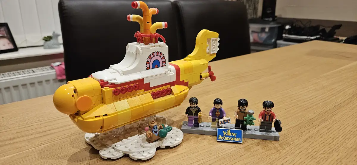 A LEGO model of the iconic Yellow Submarine from The Beatles' animated film, displayed on a wooden table with four LEGO…