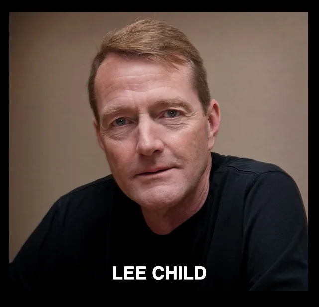 A headshot of a middle-aged white man with short brown hair and a serious expression, wearing a black t-shirt against a…