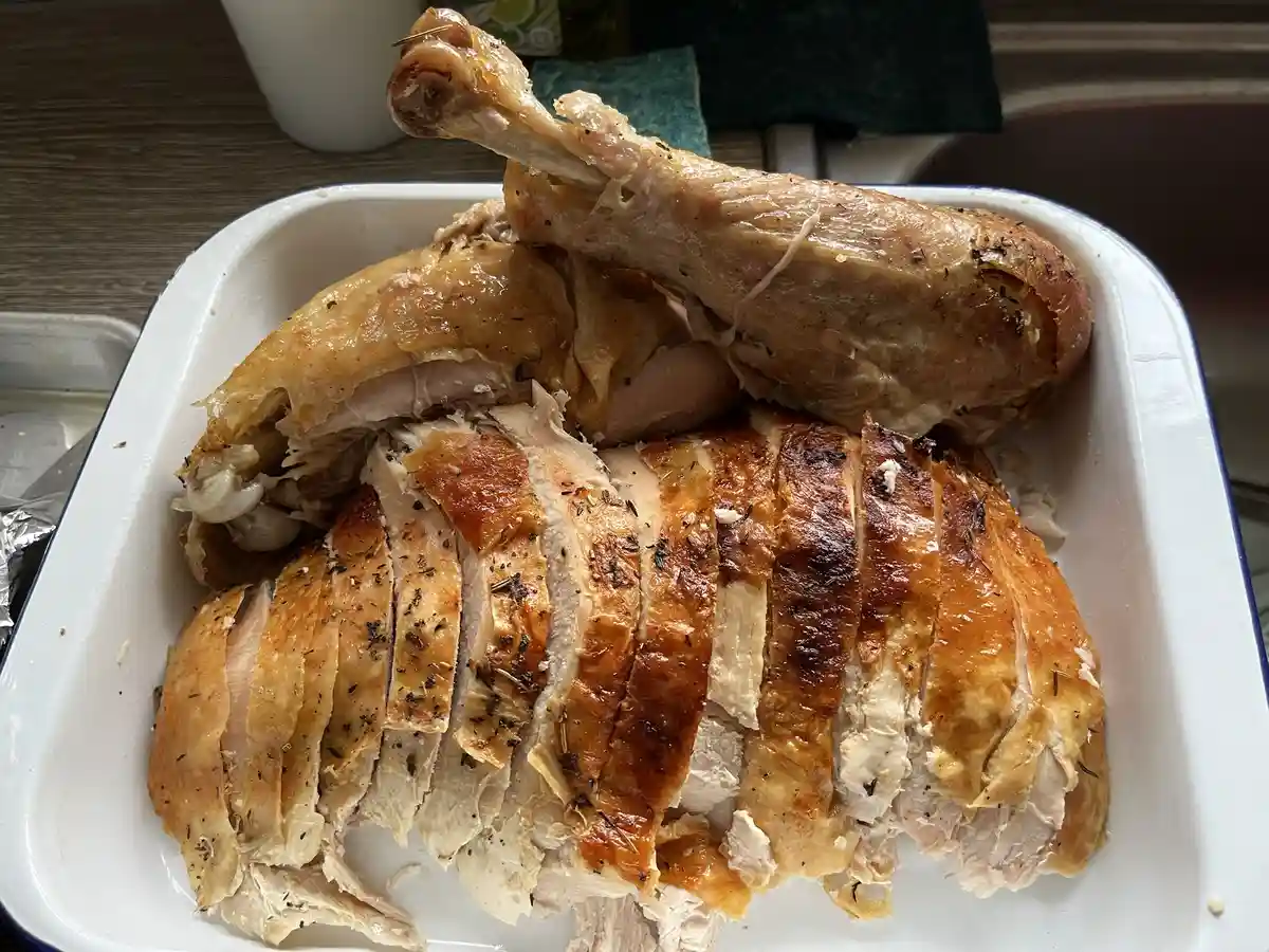 A roasted chicken is shown partially carved into slices in a white enamel dish, with the leg and thigh still attached. The…