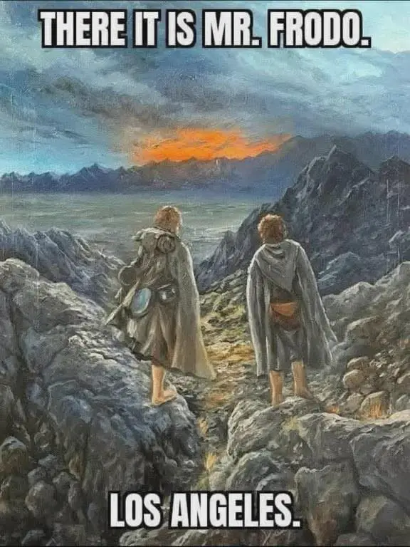Two figures stand on a rocky mountain ridge overlooking a vast valley with a dramatic sunset in the distance. The figure on…