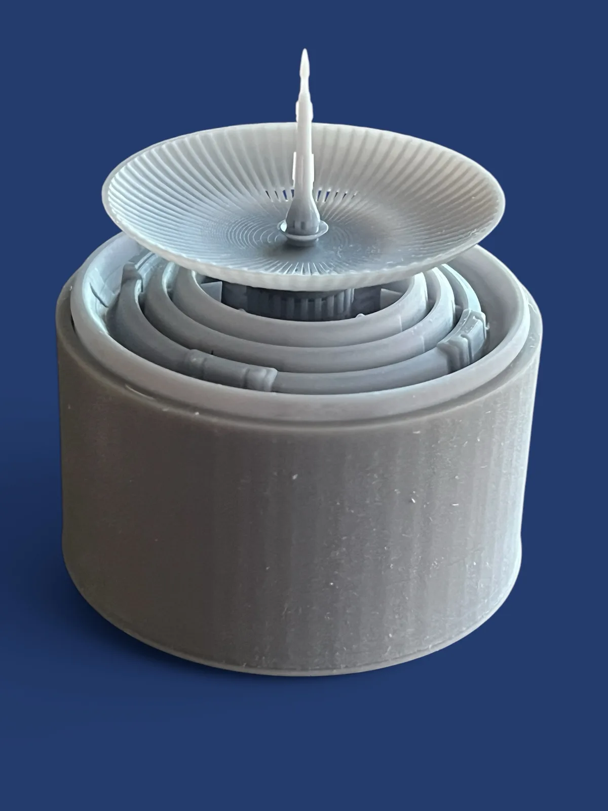 a 3d printed gray plastic model of a fountain pen nib, featuring a central spout and concentric circular ridges, sits atop a…
