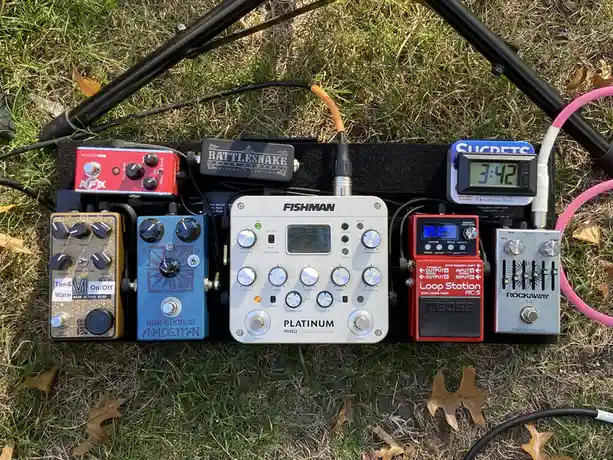 A collection of guitar effects pedals, including Fishman Platinum, Boss Loop Station, and Analog Man, are arranged on a…