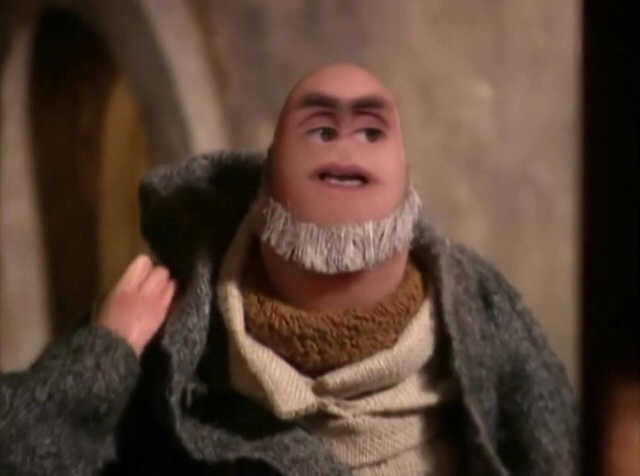 A bald, animated character with a white, fringed beard and a woolen coat looks sideways with a skeptical expression while…