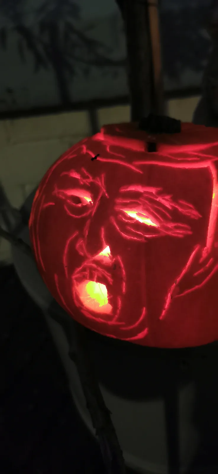 A close-up of a carved Halloween pumpkin illuminated from within, its face etched with an angry, distorted expression…