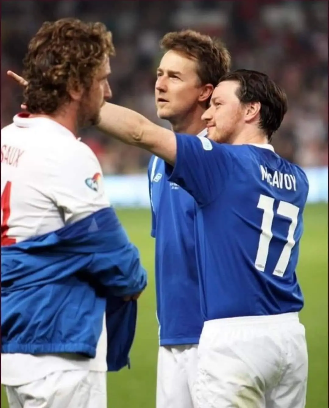 Three men in soccer uniforms on a field; one in a blue jersey with 'McAVOY 17' on the back points at another player's head…