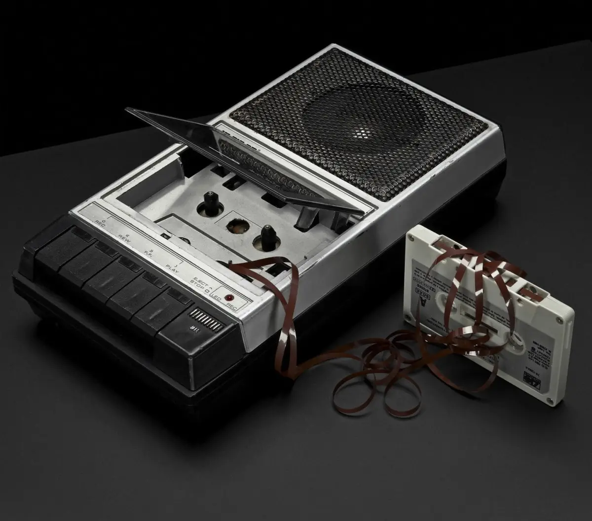 A vintage silver and black portable cassette player with its lid open, revealing empty tape reels and control buttons, sits…