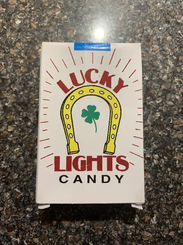 A white box of 'Lucky Lights Candy' sits on a speckled countertop, featuring a yellow horseshoe with a green four-leaf…