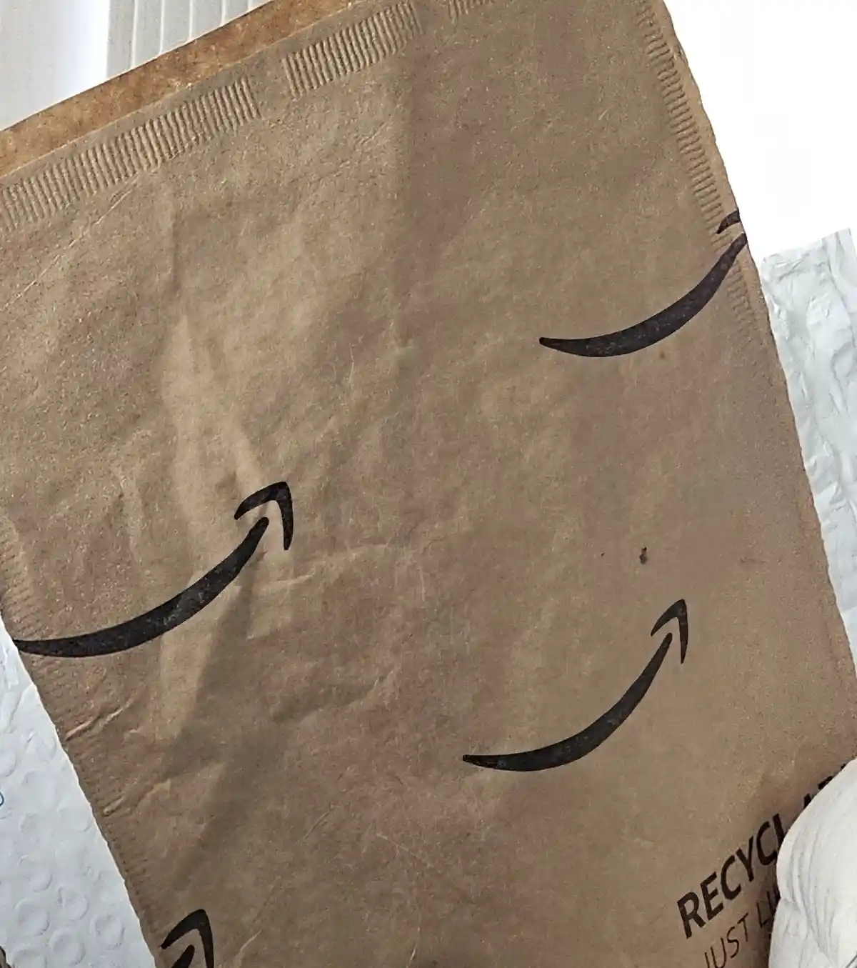 A close-up of a brown Amazon paper bag showing the company's smile logo, which is arranged to resemble a smiling face with…
