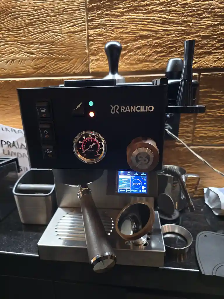 A close-up photo of a black Rancilio espresso machine on a dark countertop, with its digital display showing '19.5°C' and…