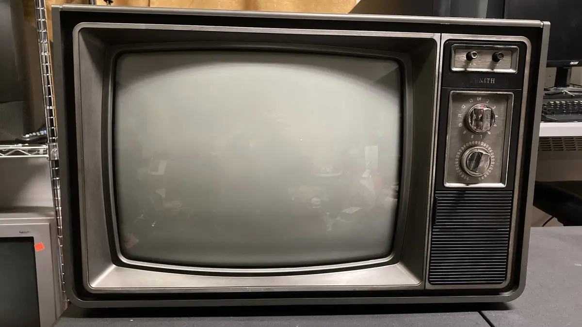 A vintage black-and-silver Zenith television with a fogged or dirty screen, showing no image, and two dials on the right…