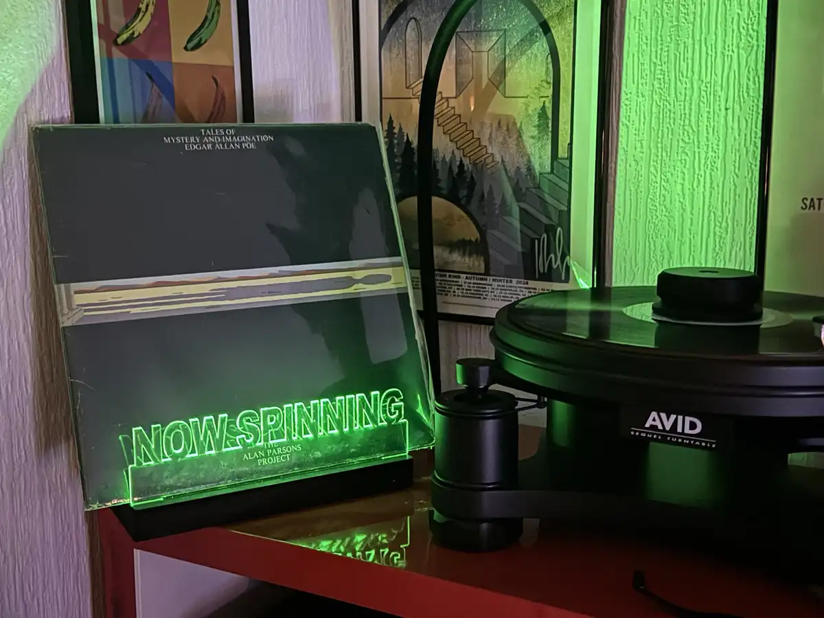 A vinyl record player with a glowing green neon sign that reads 'NOW SPINNING THE ALAN PARSONS PROJECT' sits on a red shelf…