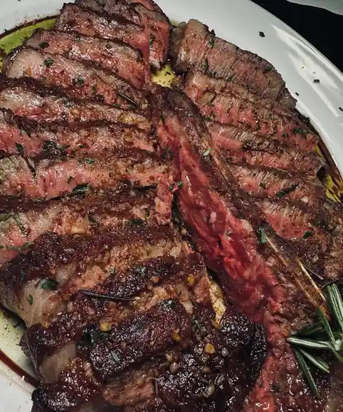 a close-up photo of a sliced, juicy, medium-rare steak on a white plate, garnished with herbs and rosemary, with overlaid…