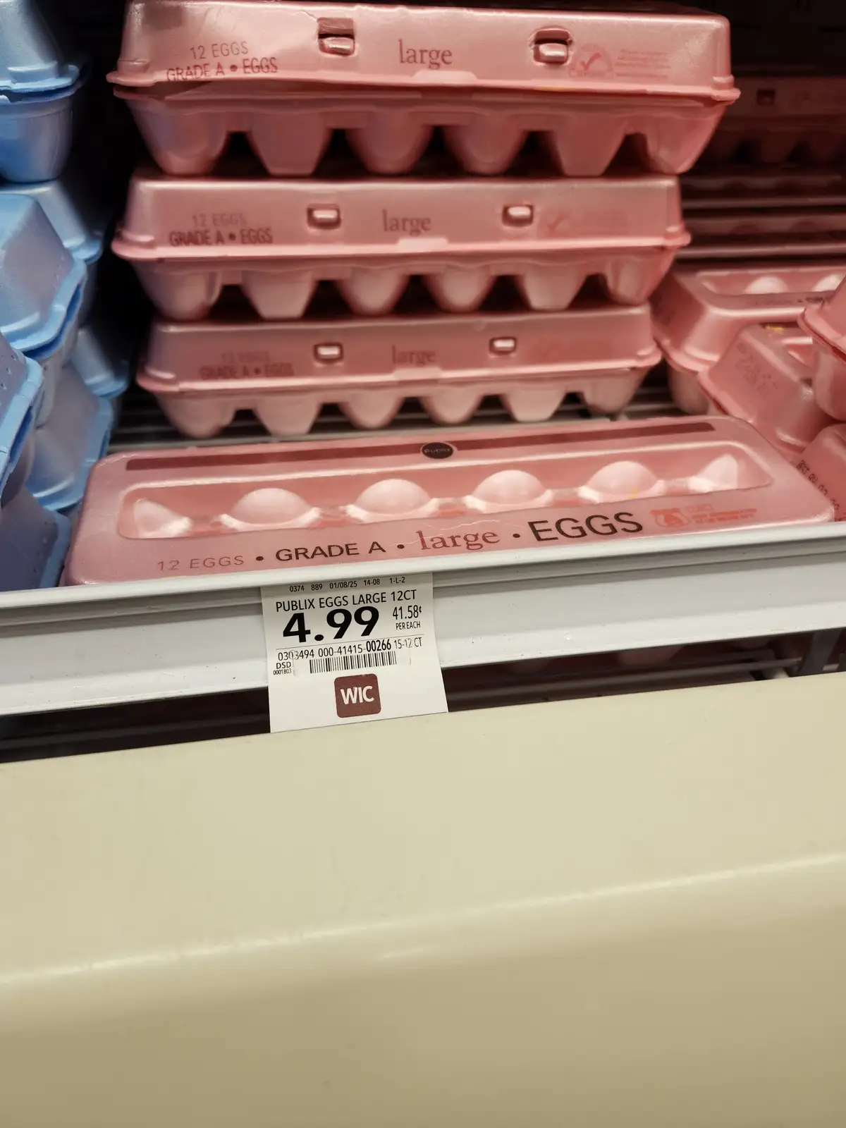 A close-up photo of a supermarket egg shelf showing pink and blue cartons of large Grade A eggs, with a price tag for Publix…