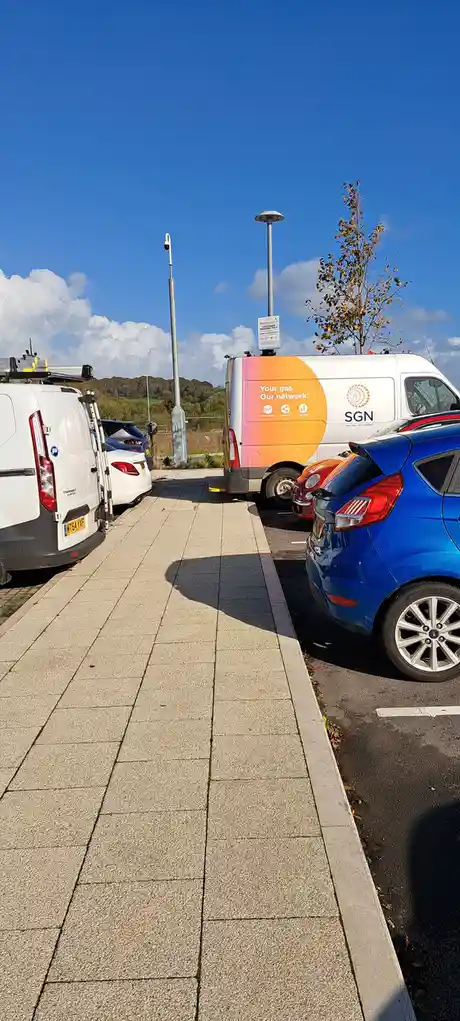 A photo of a parking lot with a white SGN van parked next to a blue car, featuring the text 'Your gas. Our network.' on its…