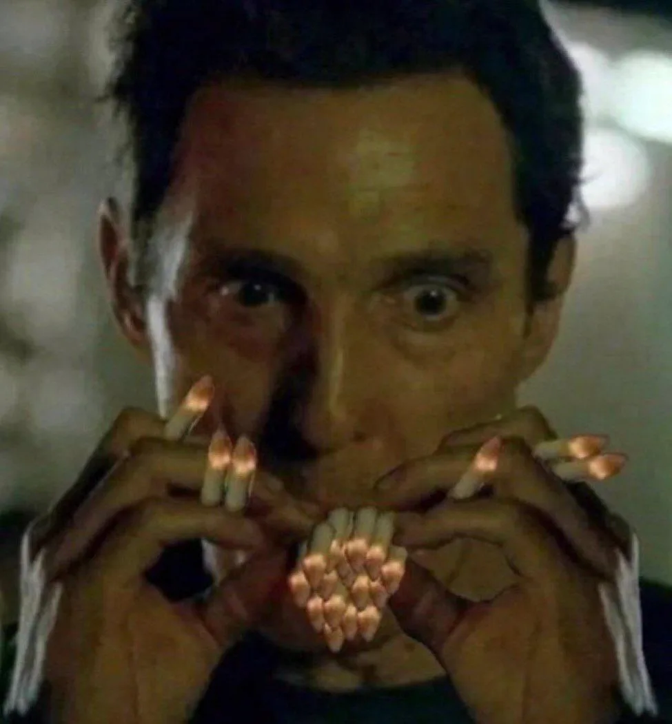 A man with wide, startled eyes holds numerous lit matches in both hands, arranged in a cluster near his mouth and nose. The…