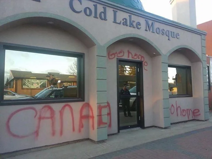 The exterior of a building labeled 'Cold Lake Mosque' has red graffiti spray-painted on its walls. Large letters spell…