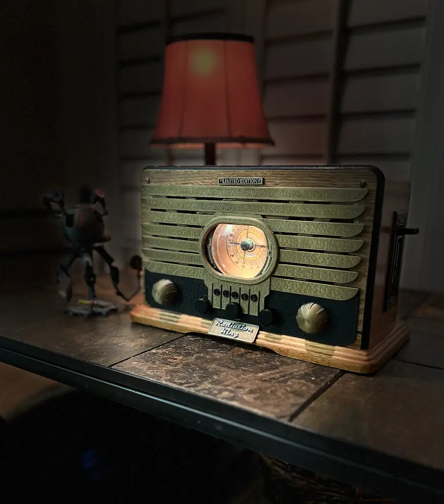 A vintage-style wooden radio with a glowing dial sits on a dark tiled surface, next to a small robot figurine and under a…