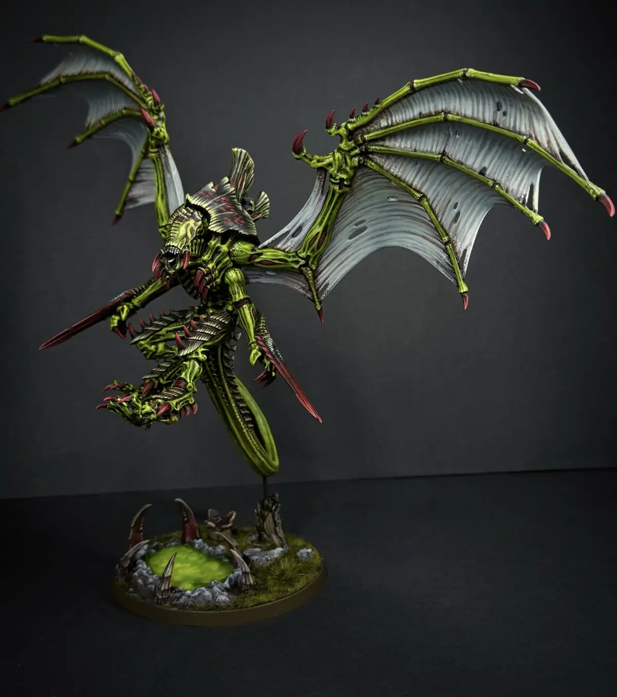 A highly detailed, green-painted miniature of a biomechanical, winged alien creature with sharp claws and spines, posed…