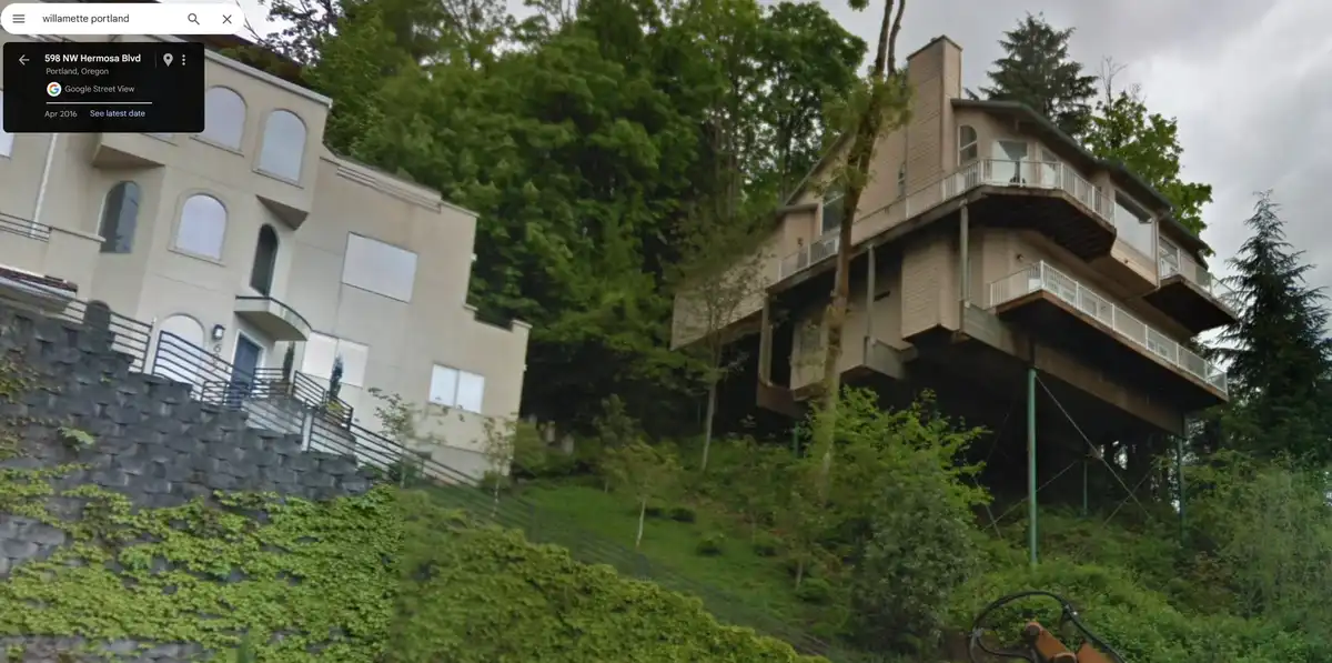 A google street view image shows two houses on a steep, tree-covered hillside in portland, oregon. The house on the right is…