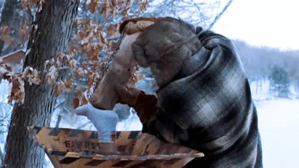 A man in a plaid shirt and blue gloves is shown in six frames, struggling to pull a large, heavy log out of a wooden sled…