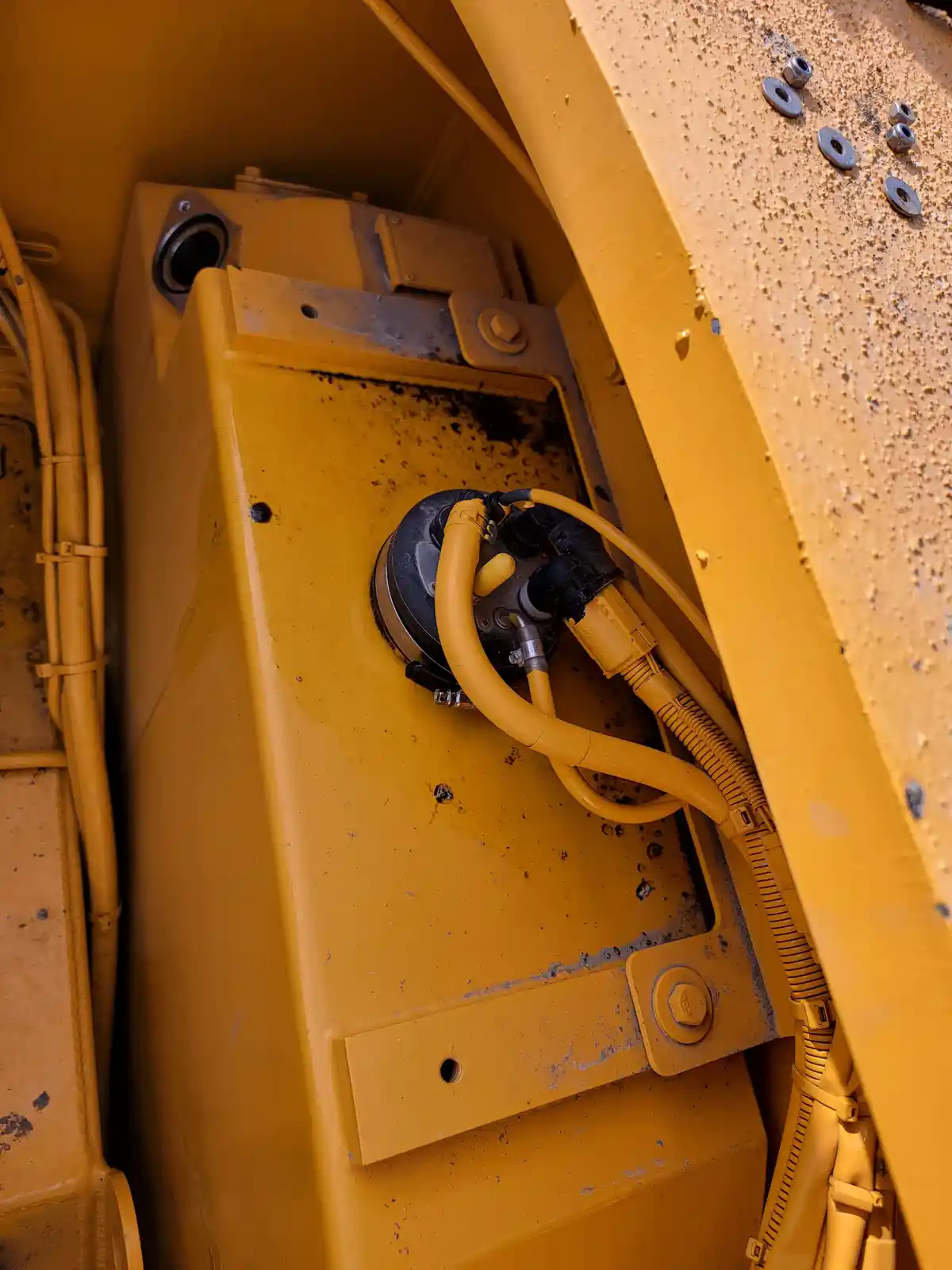 A close-up shot of a yellow industrial machine's interior, showing a dusty, grimy electrical junction box with yellow cables…