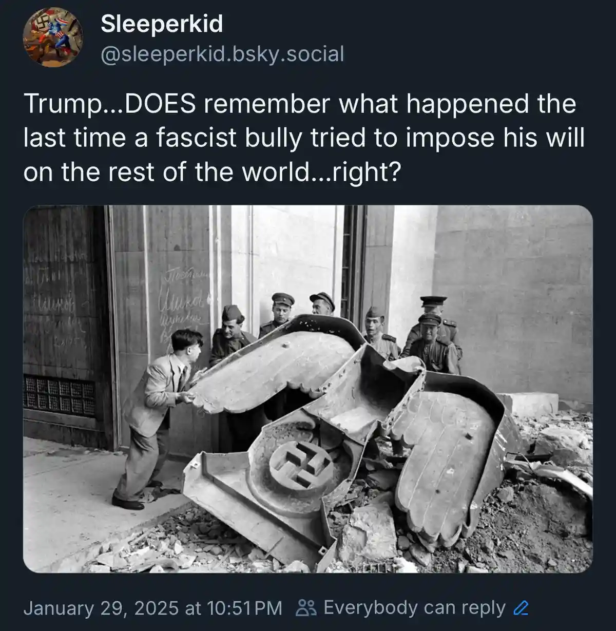 A black-and-white historical photo shows a man in a suit lifting a large, broken Nazi eagle emblem with a swastika at its…