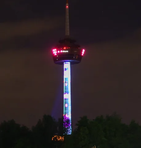 A tall, illuminated observation tower at night, its central column displaying a vertical sequence of colorful, changing…
