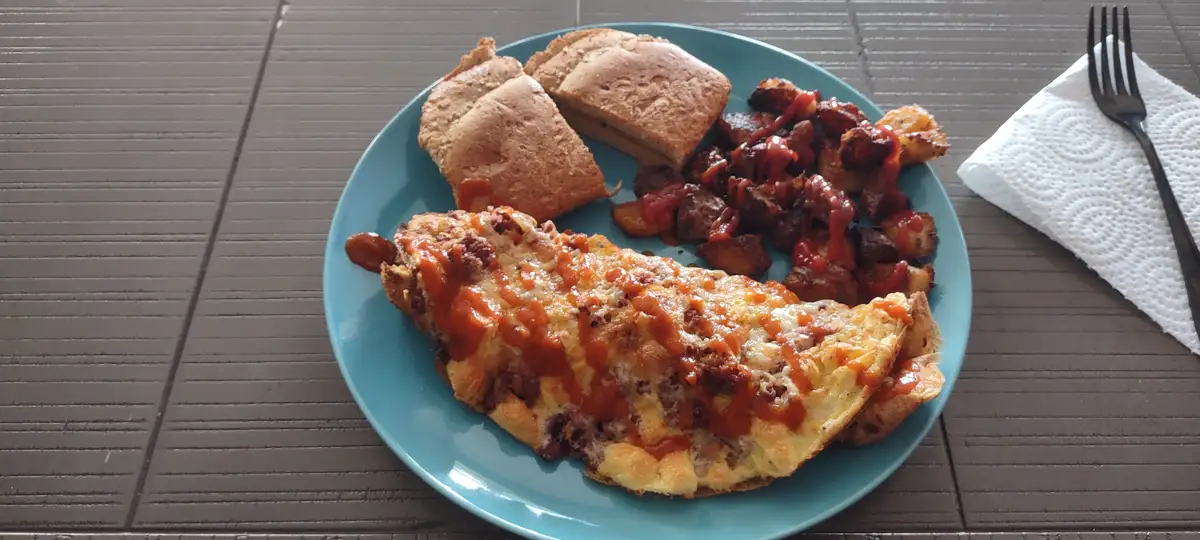 A blue plate holds a breakfast meal including an omelet with cheese and red sauce, crispy potatoes with ketchup, and two…