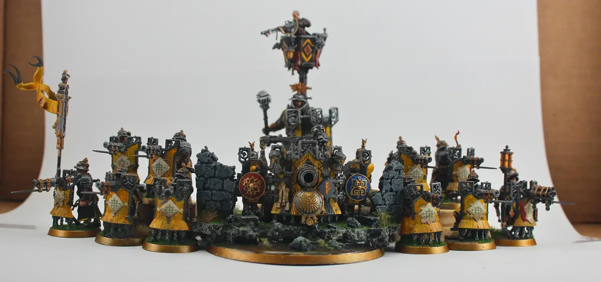 A photo of a collection of painted miniature warhammer 40k models, including infantry with shields and a large central…