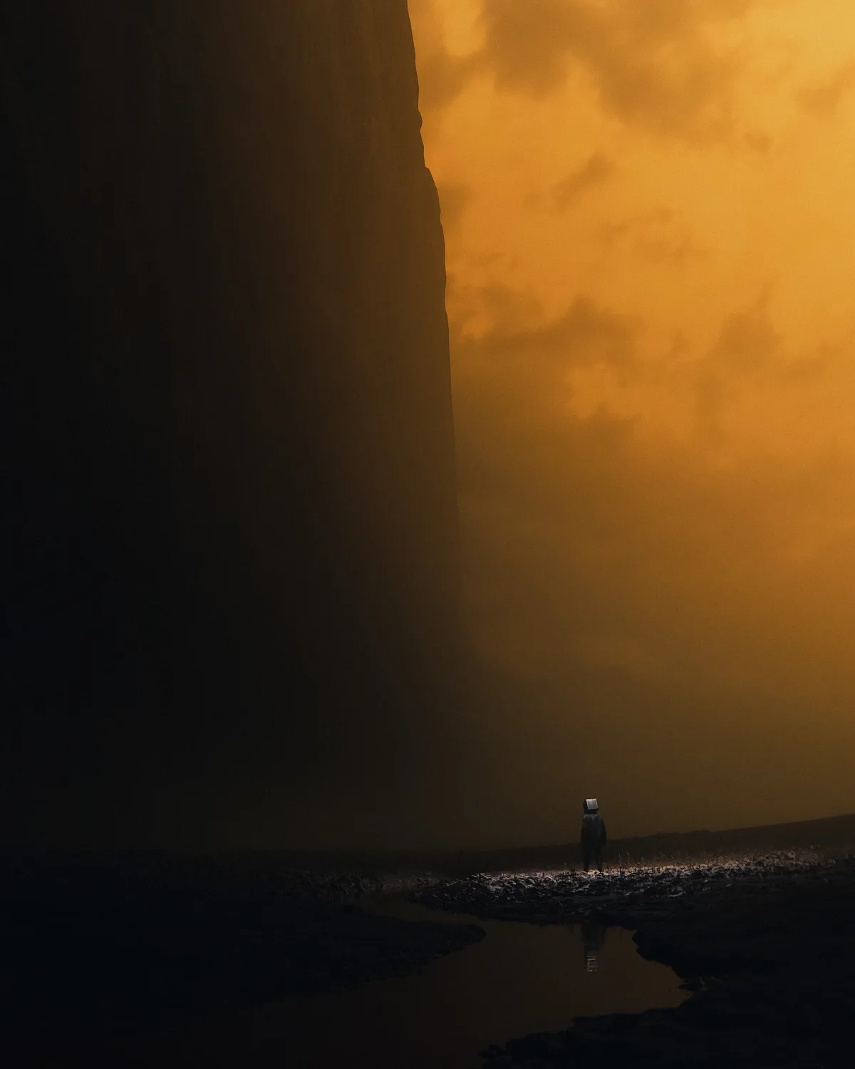 A lone figure with a box-like head stands in a desolate, orange-hued landscape beside a body of water, dwarfed by a massive…