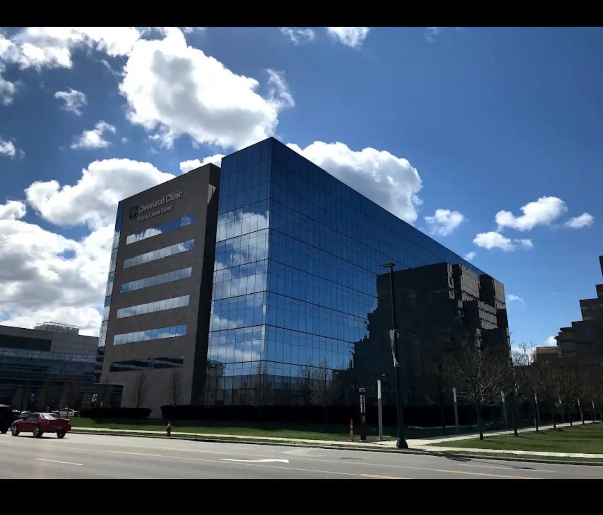 A photo of the Cleveland Clinic Testing Cancer Center building, a modern glass and stone structure under a partly cloudy…
