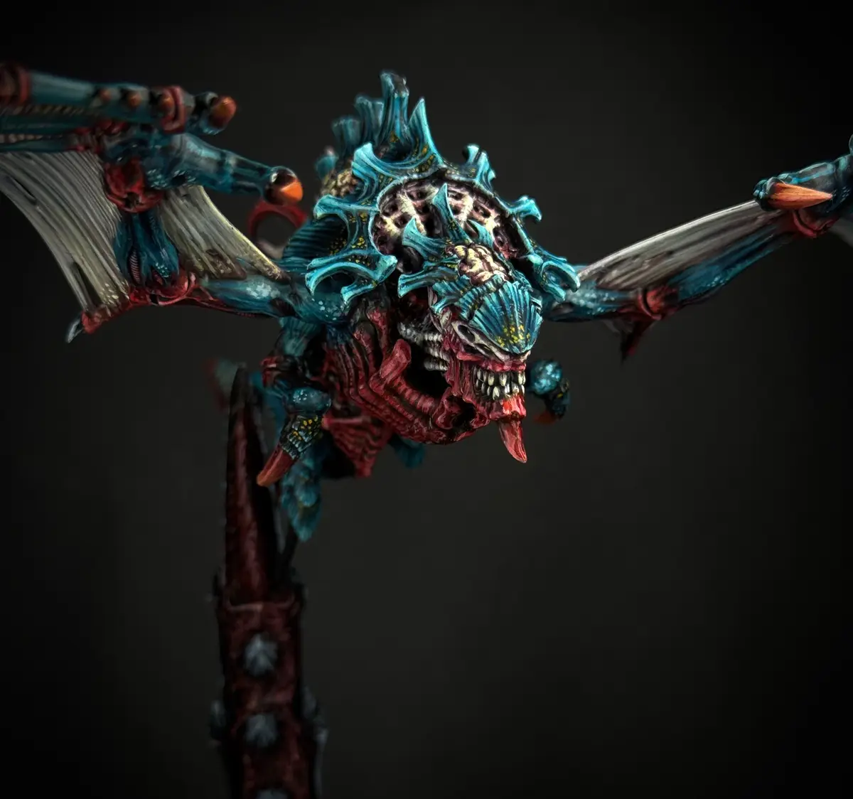 A highly detailed, painted miniature of a grotesque, biomechanical monster with blue and red coloring, sharp teeth, and…