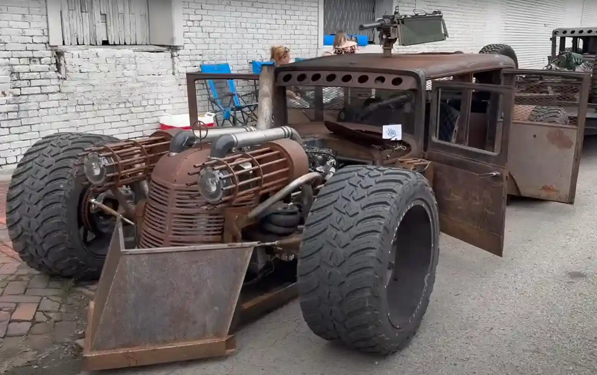 A heavily modified, rusted, and custom-built vehicle with oversized tires, exposed engine components, a front plow, and a…